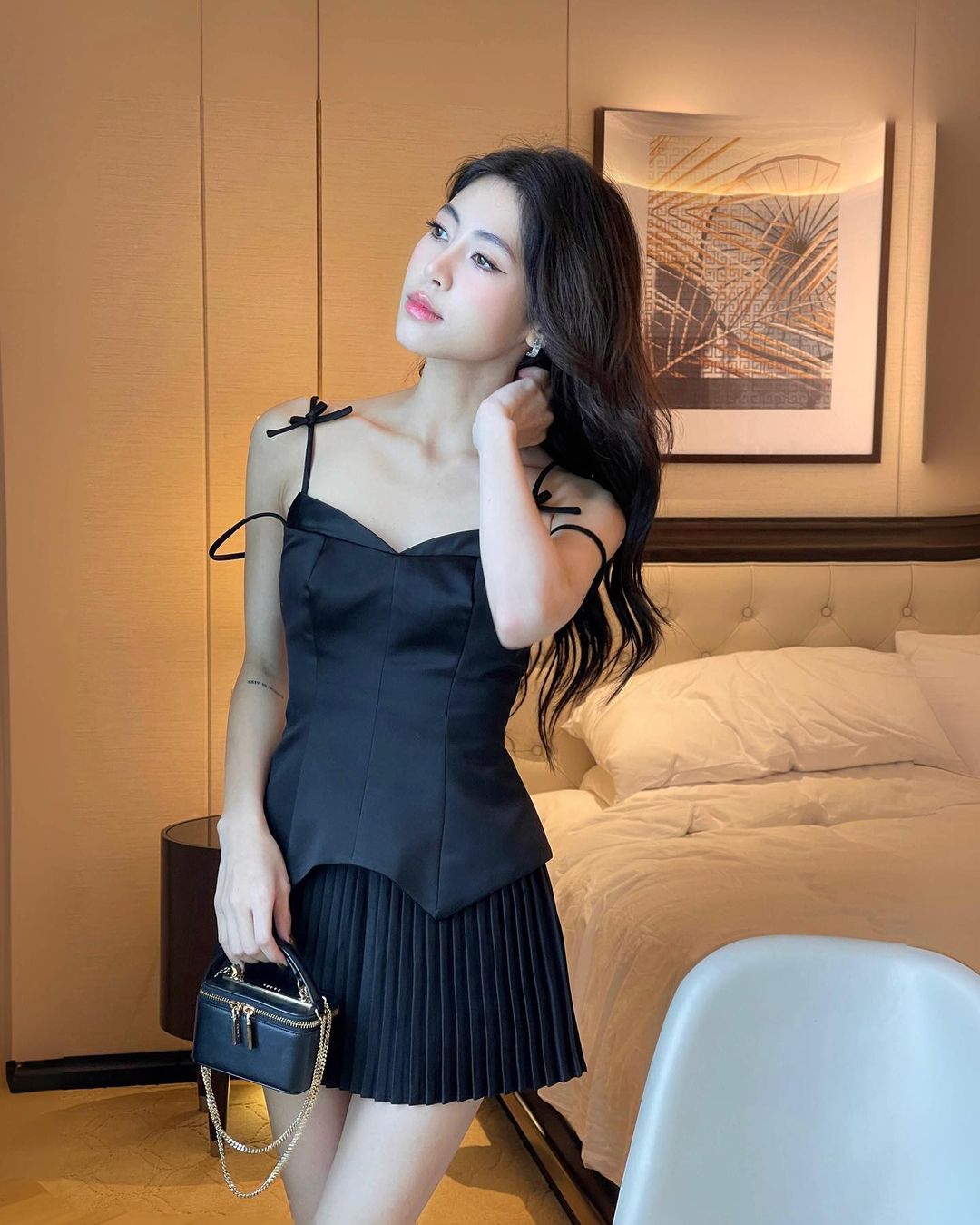 一位身穿優雅黑色鬱金香迷你裙套裝🌹、拎著小錢包的年輕女子在時尚的飯店房間裡擺姿勢。