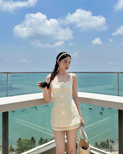 身穿 the.lookbook.select 白色 Cosmo 粗花呢裙子套裝、手持太陽眼鏡的女士站在陽台上欣賞海岸景色。