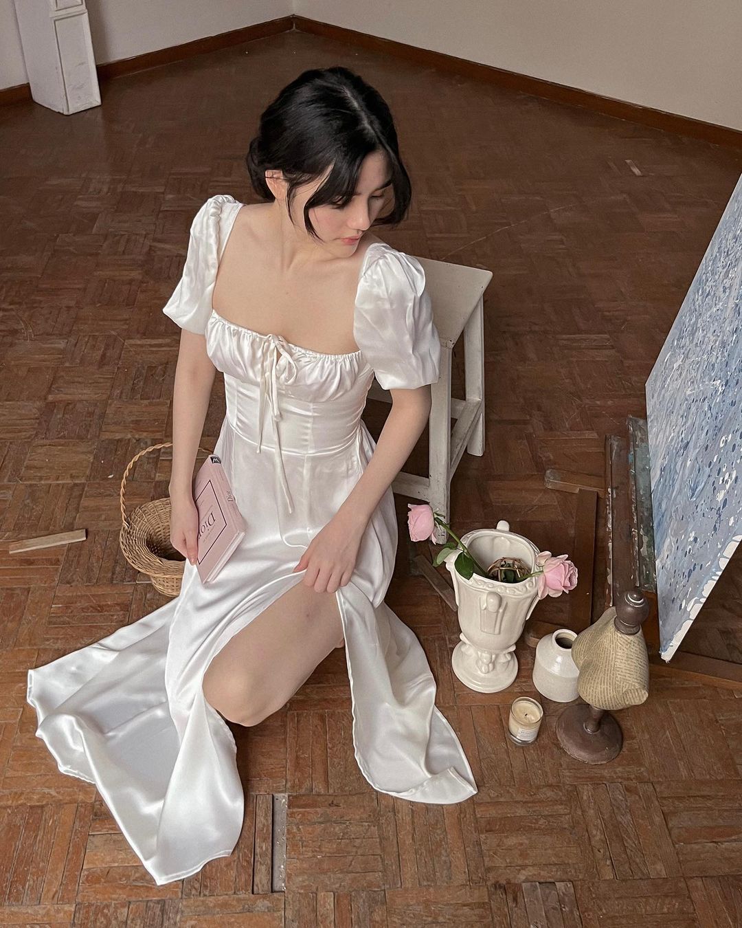 穿著 the.lookbook.select Adella 洋裝的女士坐在畫架旁邊，木地板上擺著美術用品。