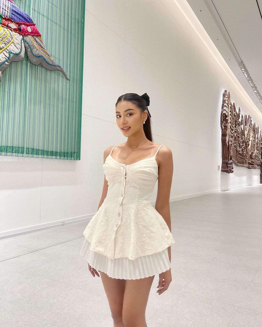 一位穿著時尚白色蘭花吊帶背心🌹倒數優惠至 5 月 19 日（來自 the.lookbook.select）的女士站在現代畫廊中，背景是大型藝術品。