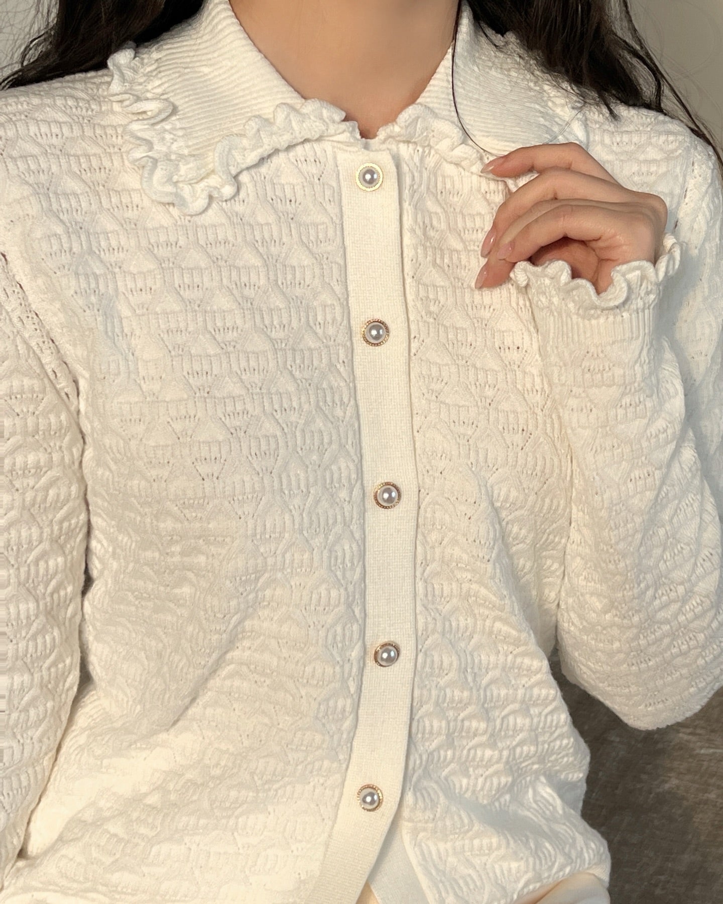 一個人穿著 the.lookbook.select 的 Janelle 針織開襟衫,具有紋理效果和優雅的褶邊領子,單手拿著 波浪花瓣領。臉部部分在畫面之外。.