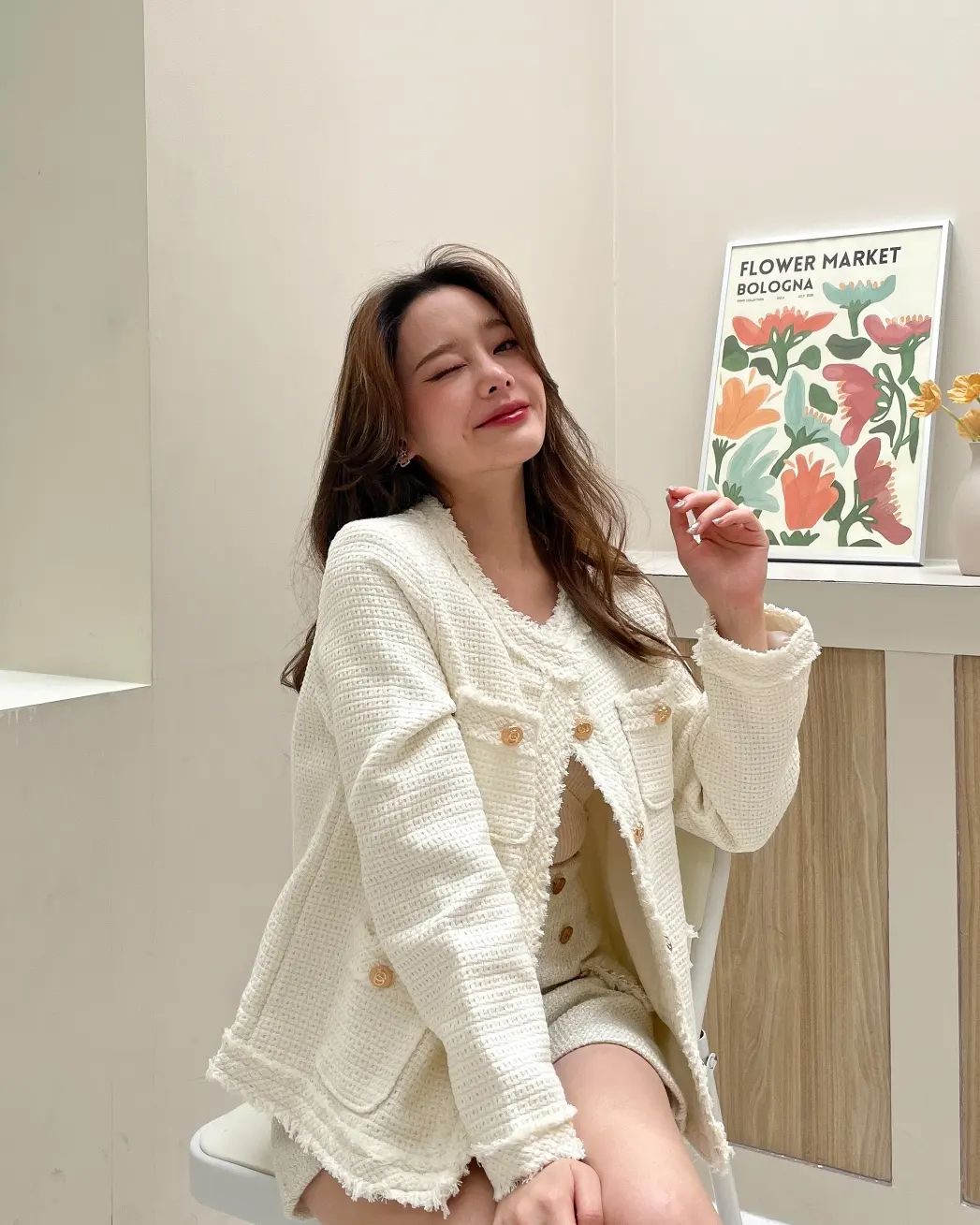 一位女士坐在椅子上,穿著 .lookbook.select 的白色粗花呢夾克和短褲。