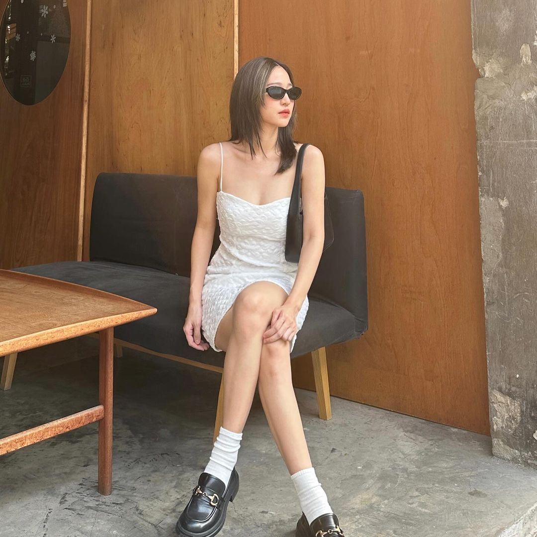 一位身穿 the.lookbook.select 設計的雛菊迷你裙的女士坐在長凳上，戴著墨鏡，置身於簡約的都市環境中。
