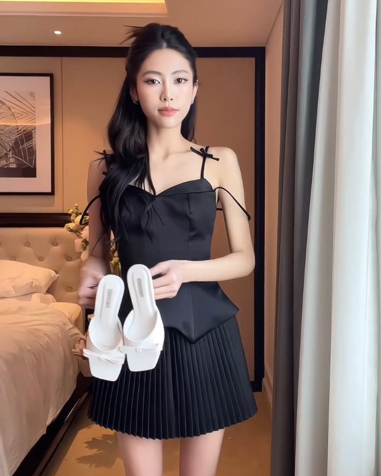 一位穿著黑色鬱金香迷你裙套裝🌹倒數優惠至5月19日和百褶裙的女士站在酒店房間裡，手裡拿著一雙來自lookbook.select的白色高跟鞋。