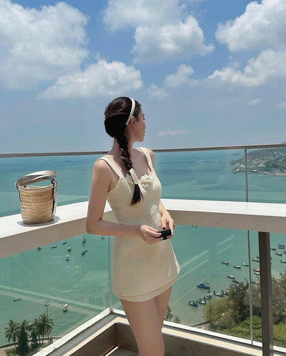 女子站在陽台俯瞰停泊船隻的海港，手持手機，身穿白色高腰連身裙，欄桿上提著小籃子，身穿 the.lookbook.select 的 Cosmo 花呢裙套裝。