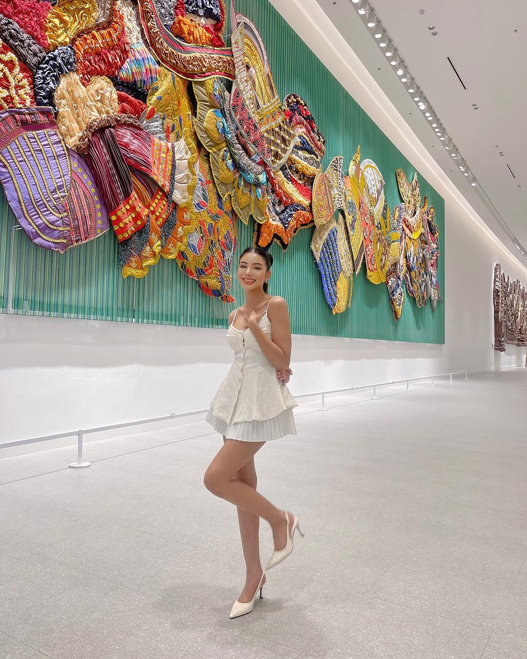 一位女士穿著 .lookbook.select 的蘭花吊帶背心和高跟鞋，在藝廊裡俏皮地擺著姿勢，身後是色彩繽紛、有紋理的牆壁雕塑。 🌹倒數優惠至5月19日