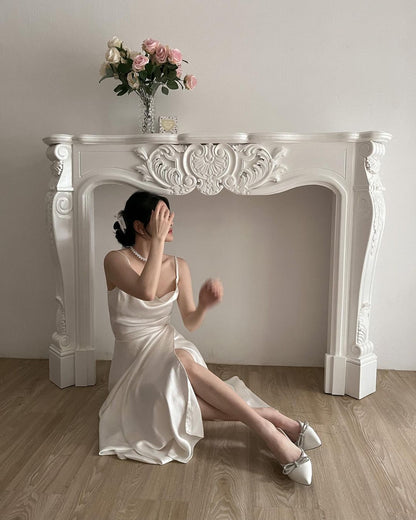 身穿白色洋裝的女士坐在華麗的壁爐旁，用手遮住臉，穿著來自 the.lookbook.select 的芭蕾舞長裹身裙。
