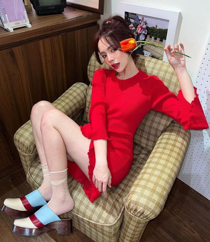 一位女士穿著 the.lookbook.select 的紅色 Belle Sleeve 針織連身裙（象牙色有貨！），坐在椅子上，手裡拿著一朵帶有鏤空細節的花朵。