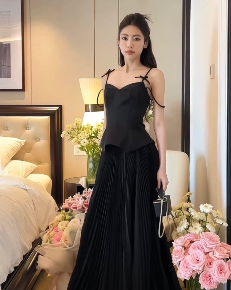 一位女士穿著優雅的黑色連身裙，搭配來自 the.lookbook.select 的鬱金香裙套裝，站在一間米色裝飾的房間裡，附近有粉紅色的玫瑰。