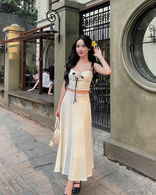 一位身穿時尚奶油色山茶花裙套裝🌹倒數優惠至5月19日服裝的女士，頭髮上別著一朵黃花，在咖啡館背景的城市街道上擺姿勢。