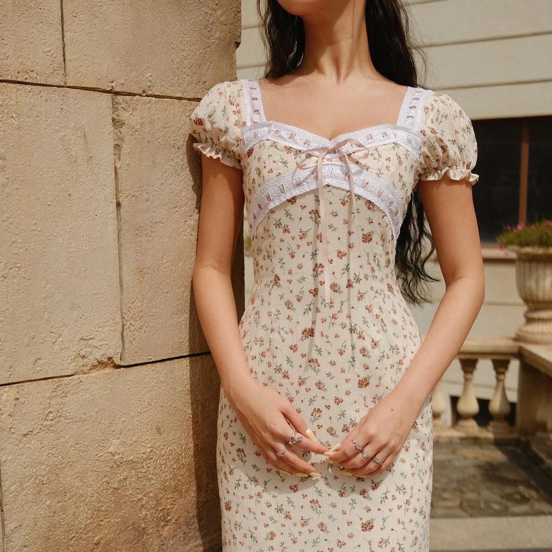 一位女士穿著 the.lookbook.select 的 Luna 連身裙,其特點是花朵圖案和泡泡短袖,站在戶外石牆旁邊,雙手緊握在一起。 (🛒新品限量時優惠•9月30日結束)