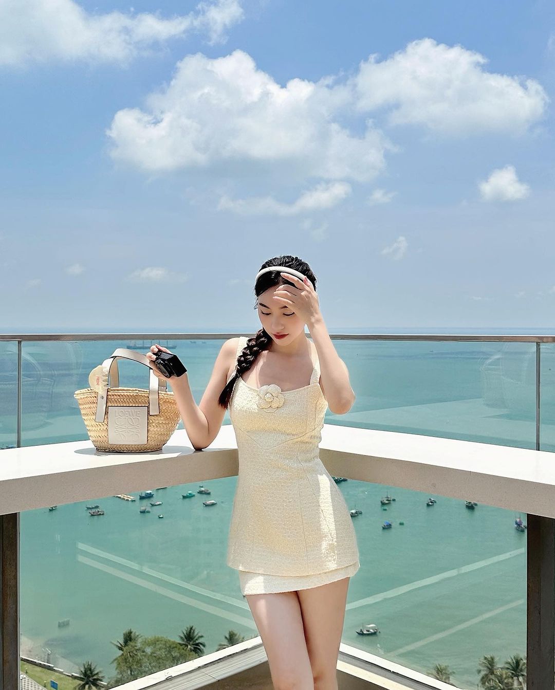 一位身穿黃色高腰連身裙的女士，手持 the.lookbook.select 出品的 Cosmo 粗花呢裙套裝，站在陽台上欣賞蔚藍的大海和船隻。 🌹倒數優惠至5月19日