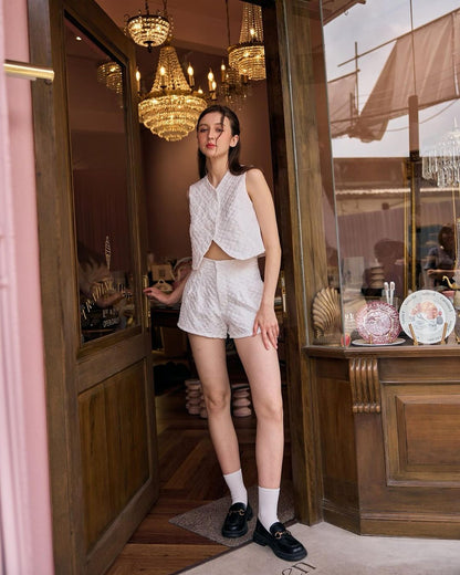 一位穿著時尚白色服裝的女士站在優雅商店的門口，一隻手放在門上，穿著來自 the.lookbook.select 的 Daisy 短褲套裝。 🌹倒數優惠至5月19日