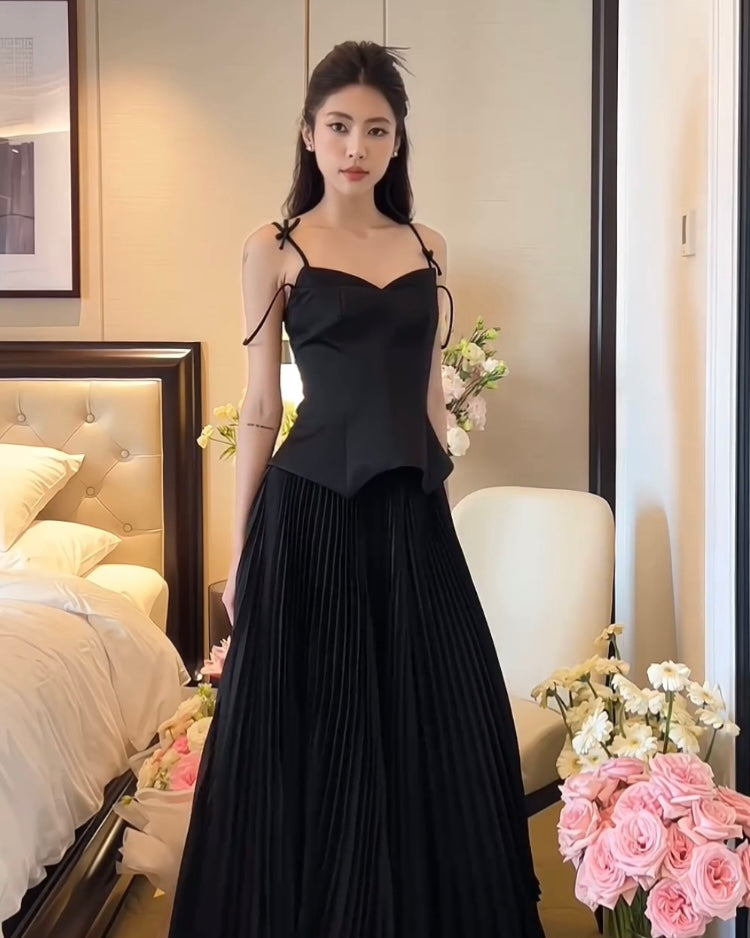 一位女士穿著優雅的細肩帶黑色連身裙和 the.lookbook.select 鬱金香裙套裝，站在房間裡，房間裡擺著鮮花，背景是一張豪華床。