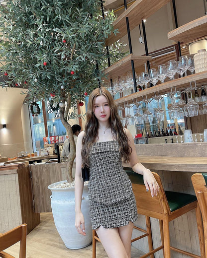 一位穿著由 the.lookbook.select 出品的茉莉花呢裙子套裝的年輕女子站在一家現代咖啡館內的盆栽橄欖樹旁，背景是架子上的眼鏡。