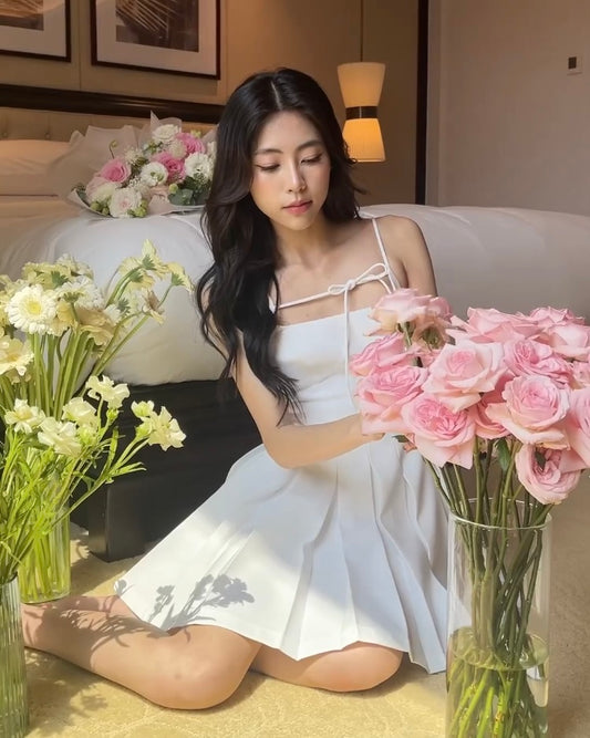 一位穿著 the.lookbook.select 的 Lily 迷你裙的女士坐在地板上，在裝飾典雅的酒店房間裡擺放粉紅玫瑰。