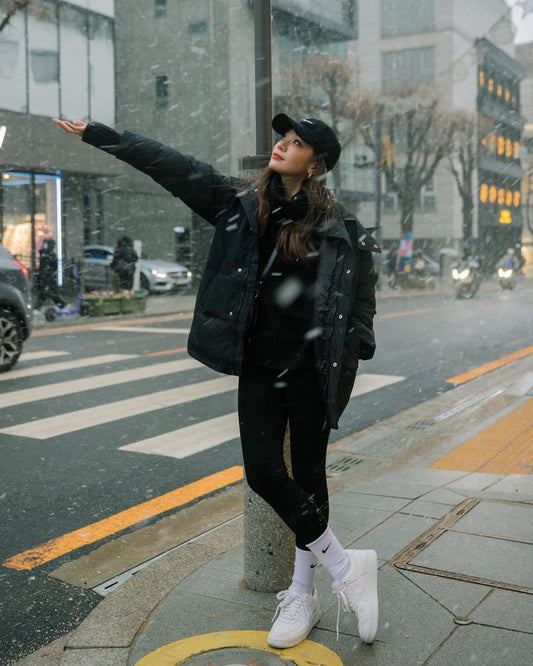 一位女士穿著保暖緊身褲和 the.lookbook.select 的大羽絨服，在雪地街道上擺姿勢。