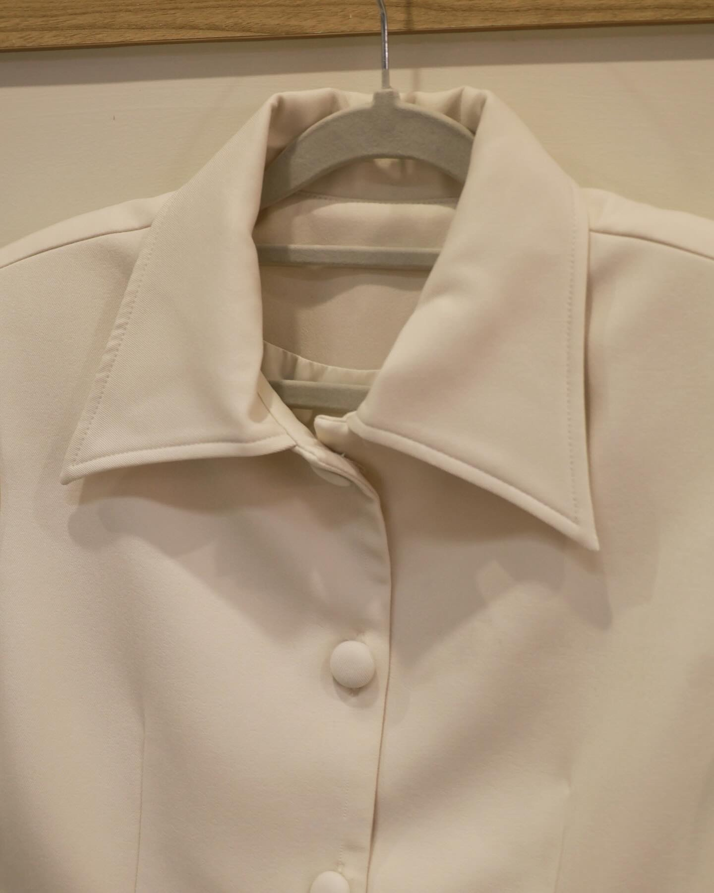 The.lookbook.select的乳白色輕質短裙套裝特寫，展示在衣架上的布料包覆的大釦子和經典的立領設計。.