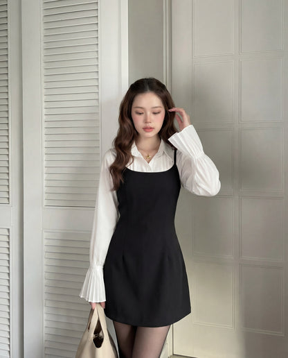 在室內，一位女士穿著 the.lookbook.select 的 Muse Cami 連身裙，搭配袖口有褶的白色上衣，手拿米色包包，一隻手靠近頭髮向下凝視。.
