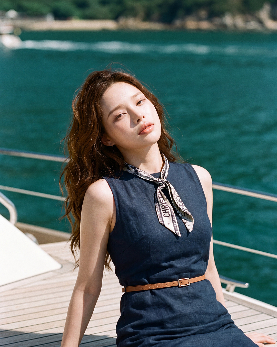 一位長髮女子身穿 the.lookbook.select 的「卡普里繫帶迷你洋裝」，坐在船甲板上，背景可見水面與樹木。.