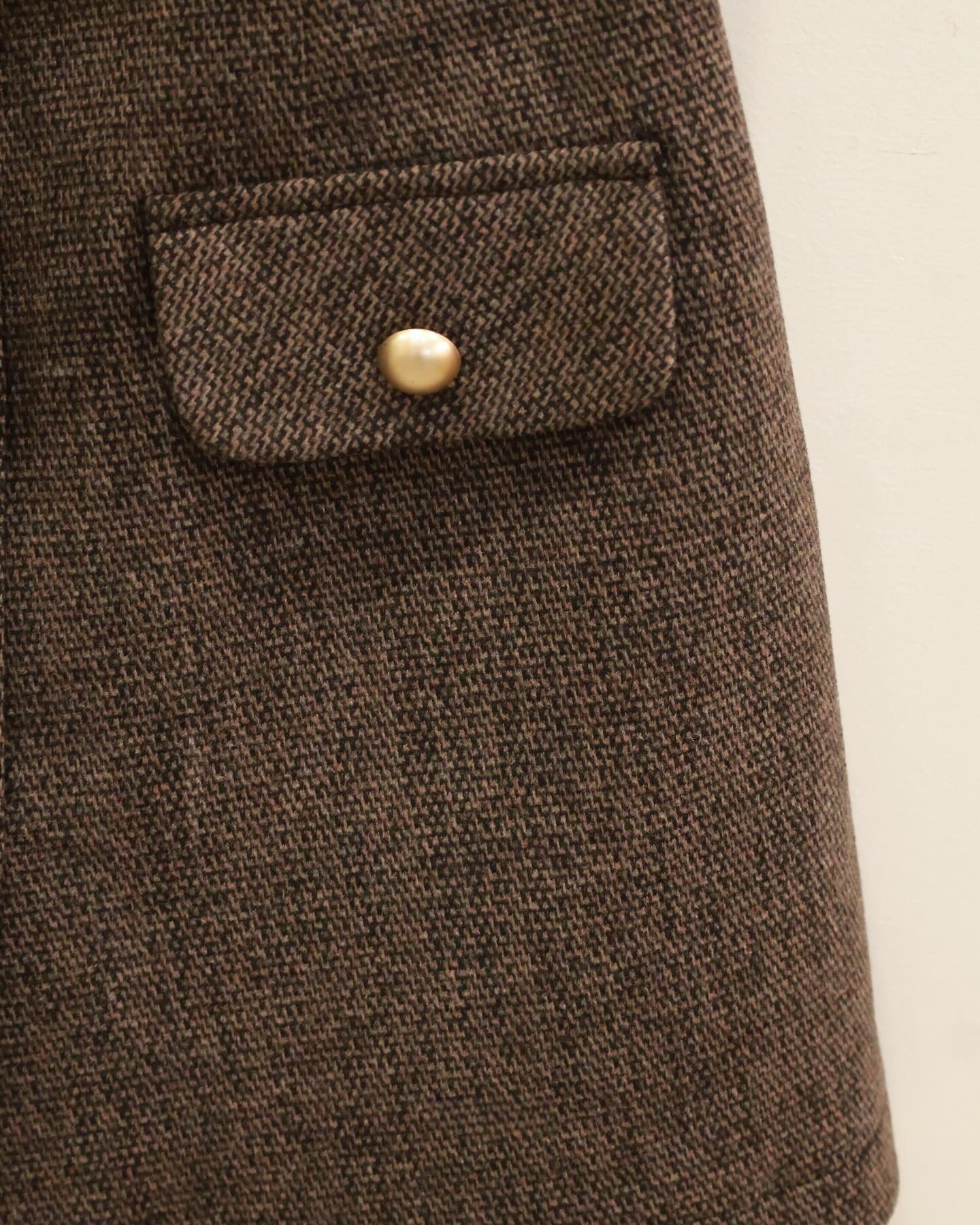 The.lookbook.select的Moka粗花呢連衣裙特寫，以棕色粗花呢布料口袋為特色，配上翻蓋和圓形金色鈕扣，襯托素雅的淺色背景。🖤新品優惠2件9折.