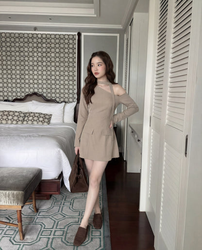 一位身穿 the.lookbook.select 單肩西裝連衣裙的女士站在現代化的臥室中，手持棕色手提包，床、長椅和花紋地毯清晰可見。.