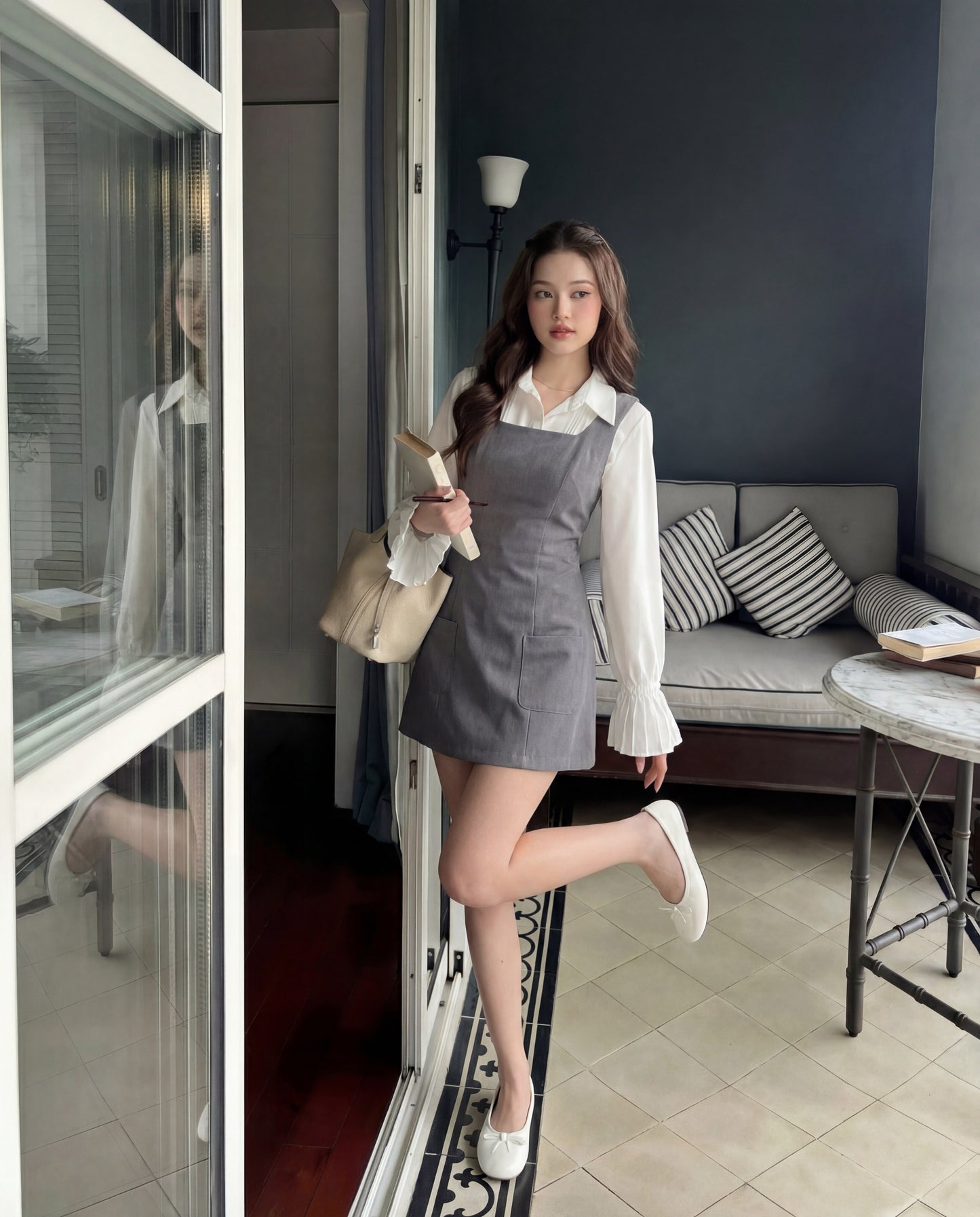 一位身穿白色上衣和 the.lookbook.select's Junior Sleeveless Dress 的女士站在玻璃門旁，手上拿著一個米色袋子，背景是沙發和桌子。.