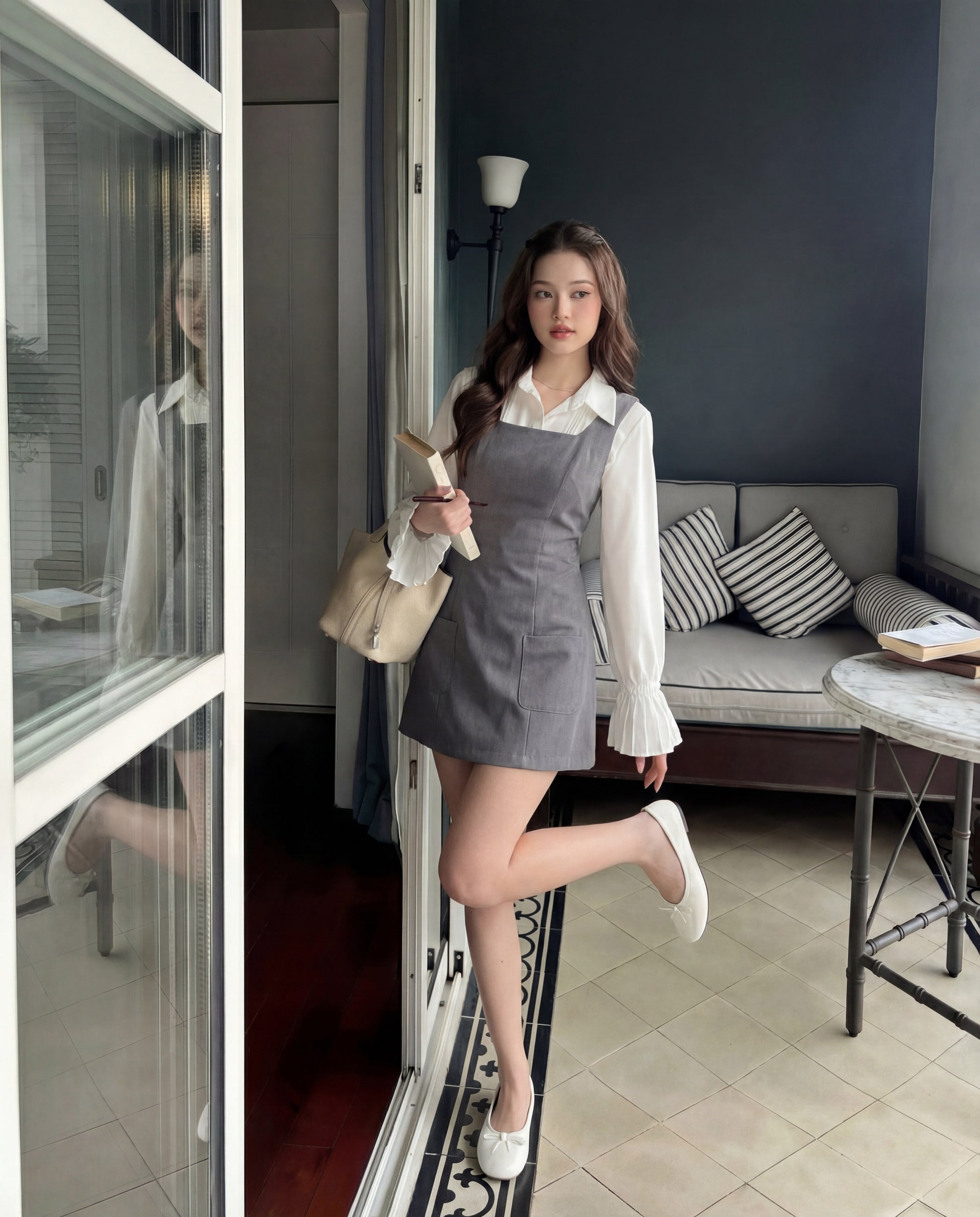 一位身穿白色上衣和 the.lookbook.select's Junior Sleeveless Dress 的女士站在玻璃門旁，手上拿著一個米色袋子，背景是沙發和桌子。.