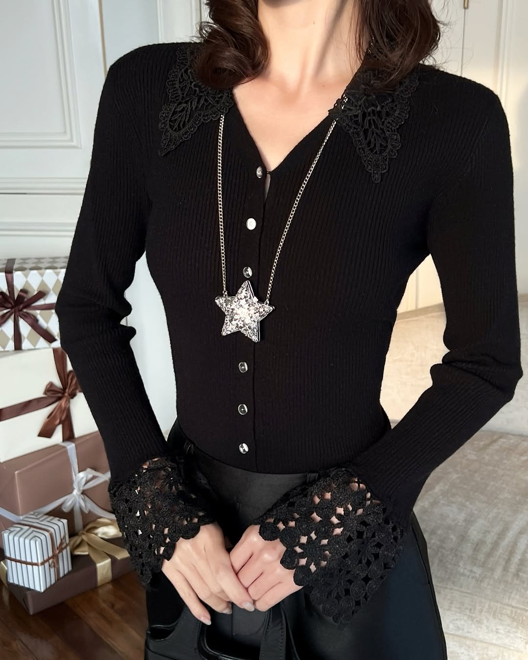 A person wars the.lookbook.select's Lace Knit Top❄️新品優惠-黑色蕾絲領口和袖口、銀色鈕釦和星星吊墜項鏈，站在包裝好的禮盒旁。.