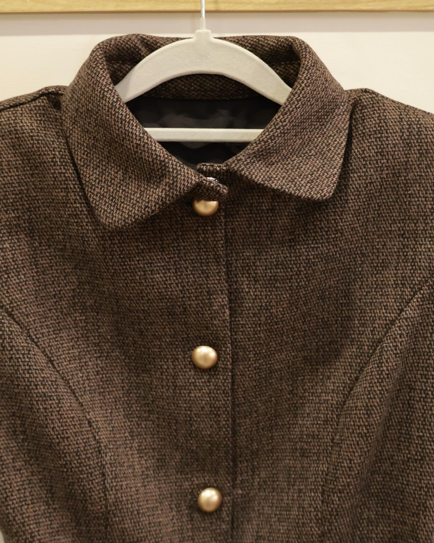 The.lookbook.select的 Moka Tweed Dress 🖤新品優惠2件9折掛在衣架上的特寫，展示其棕色紋理布料、衣領和前襟的三顆金色鈕扣。.