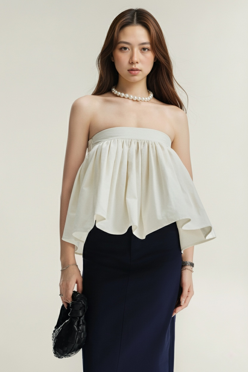 一位身穿白色露肩上衣、珍珠項鍊和手鐲的女士，手持黑色編織手拿包，同時穿著 the.lookbook.select 的 Jesse 迷你裙，站在淺色背景下。.