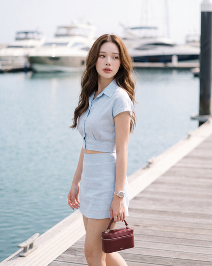 一位女子身穿 the.lookbook.select 的「Breeze 亞麻套裝」，站在水邊的碼頭上，手拿一個小巧的酒紅色手提包，背景中可見遊艇。.