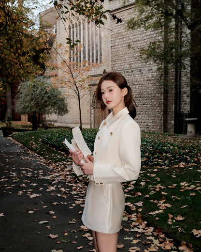 The.lookbook.select的Grace Little Jacket 🖤新品優惠至12月5日，一位女士站在戶外落葉鋪成的小路上，手持一本打開的書，背景是石頭建築和樹木。.