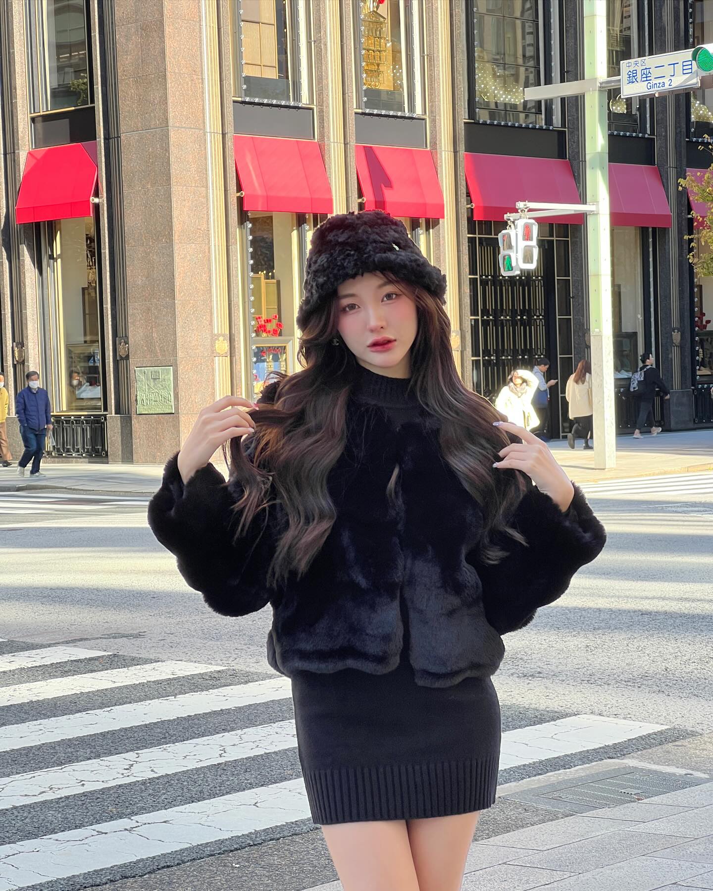 一位穿著 the.lookbook.select Marshmallow Fur Coat (with Hat) 的女士站在城市的人行道上，背景是紅色的遮陽篷和行人。.