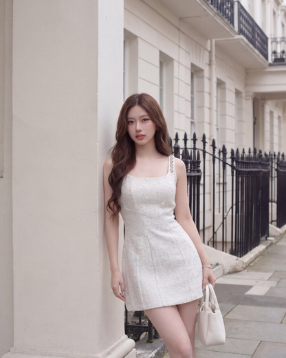 一位身穿 the.lookbook.select's Jewel Tweed Dress 🌙新品優惠2件9折的女士站在一幢輕型建築旁，手持白色手提包，背景是鐵欄杆和鋪好的人行道。.