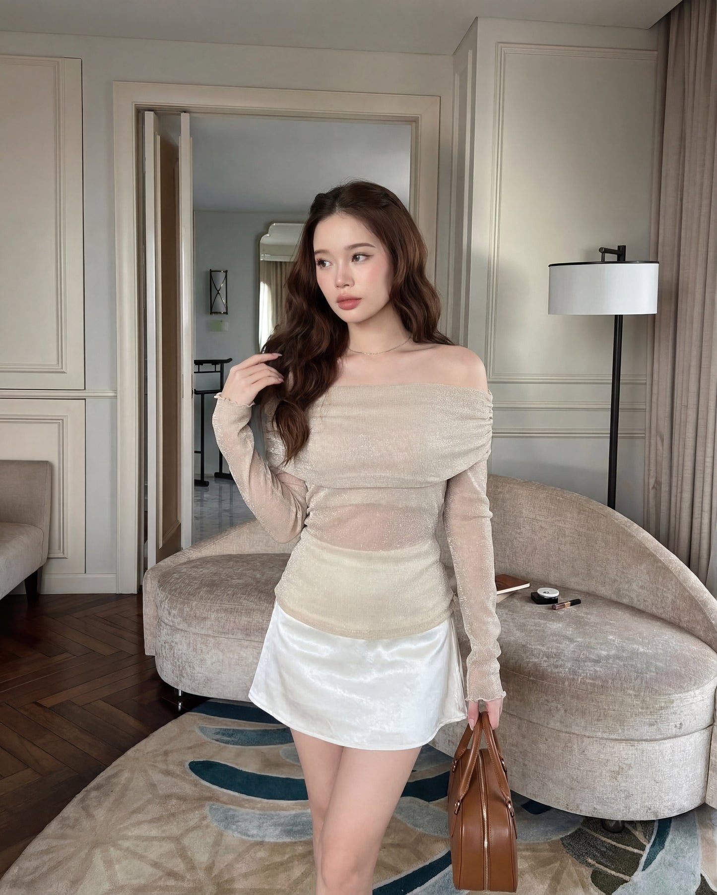 一位女士身穿 the.lookbook.select 的 Dew Knit Top 🌙新品優惠2件9折，米色配白色短裙，手持棕色手提包，置身於室內中性色調的家具和裝飾之中。.