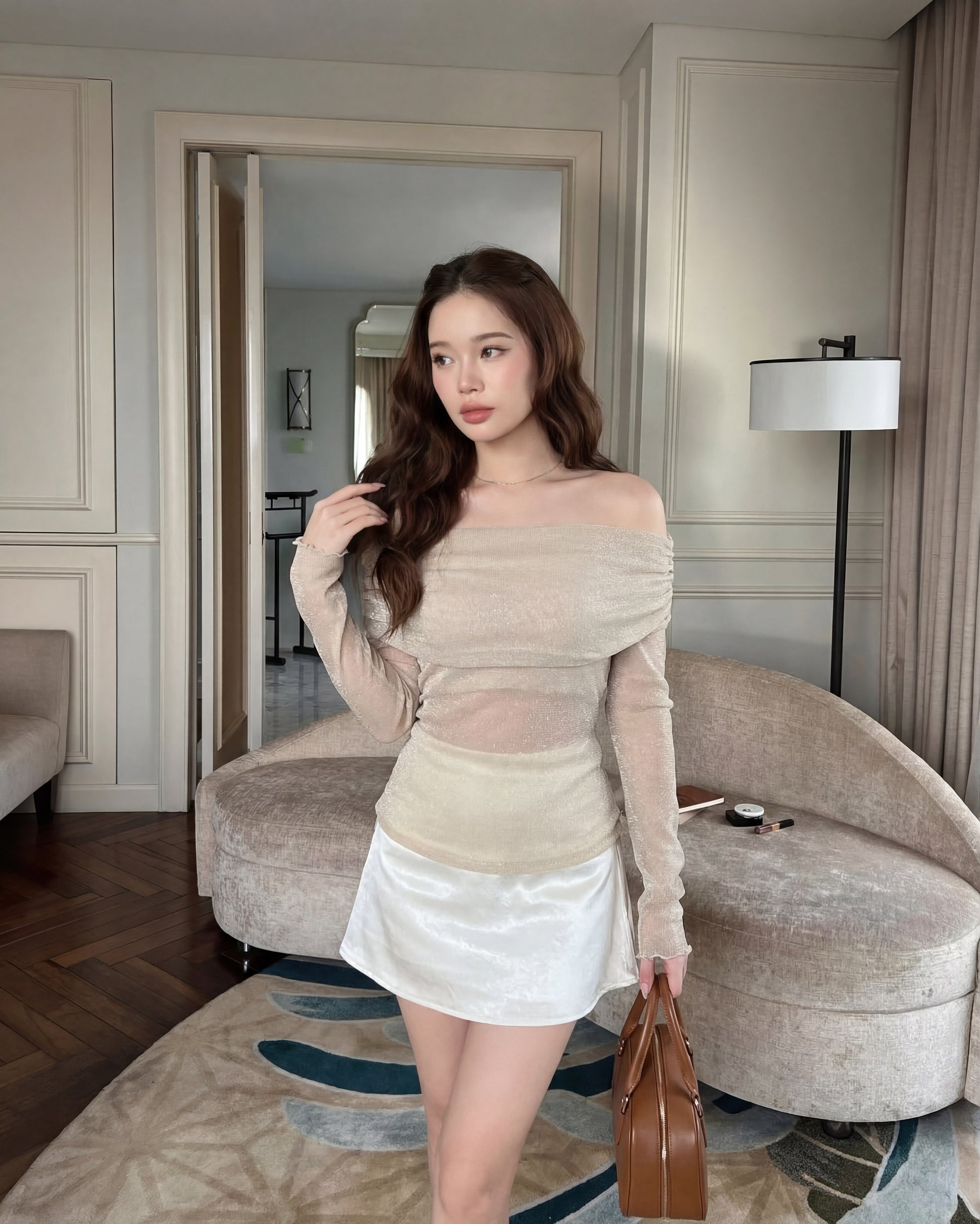 一位女士身穿 the.lookbook.select 的 Dew Knit Top 🌙新品優惠2件9折，米色配白色短裙，手持棕色手提包，置身於室內中性色調的家具和裝飾之中。.
