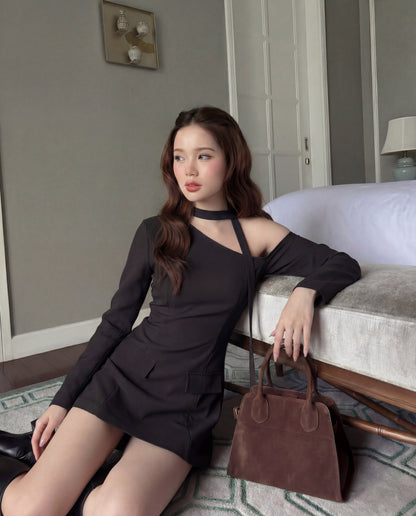 一位身穿 the.lookbook.select 單肩西裝連衣裙的女士坐在床邊的地板上，手臂靠在床上，身旁放著一個棕色手提包。.