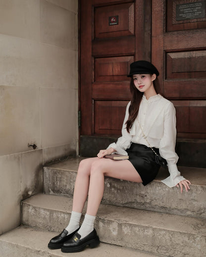 一位女士穿著 the.lookbook.select 的 Hazel White Shirt，搭配黑色短裙和帽子，優雅地坐在木門前的石階上，對著鏡頭擺出法式氣質的造型。🖤新品優惠至12月5日.