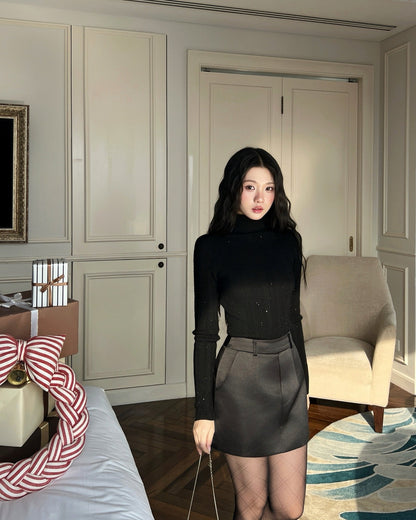 一位深色長髮的女士穿著 the.lookbook.select's Twinkle Knit Top❄️新品優惠、黑色短裙和魚網襪褲，站在光線充足的現代房間扶手椅旁。.