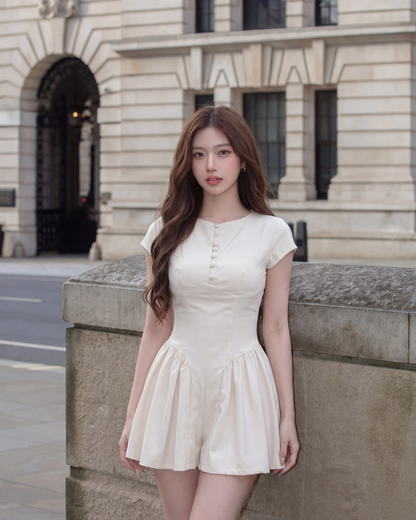 一位棕色長髮的女士穿著 the.lookbook.select 的 Berkeley Pleat 連身衣，站在石牆和歷史建築前。.