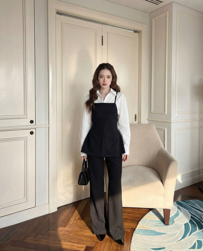 在室內的米色扶手椅旁，一位女士穿著 the.lookbook.select 的 Moet Pants Set，這是一套優雅簡約的黑色服飾，搭配結構感長褲和 Hepburn 風格的無袖上衣，再搭配黑色小手包。.