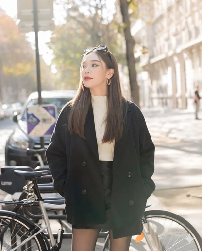 在陽光明媚的城市街道上，一位身著lookbook.select's Wool Fit Blazer的女性站在停放著腳踏車、樹木和建築物附近，展現保暖與時尚兼具的魅力。.