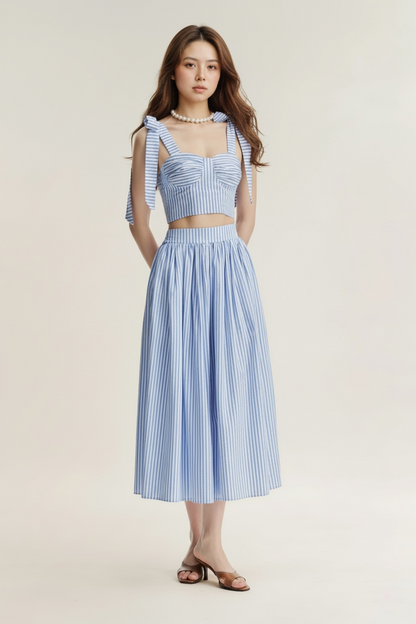 一位女士穿著.lookbook.select Jesse Maxi Skirt，搭配藍白條紋無袖束帶蝴蝶結上衣、涼鞋和珍珠項鍊。.