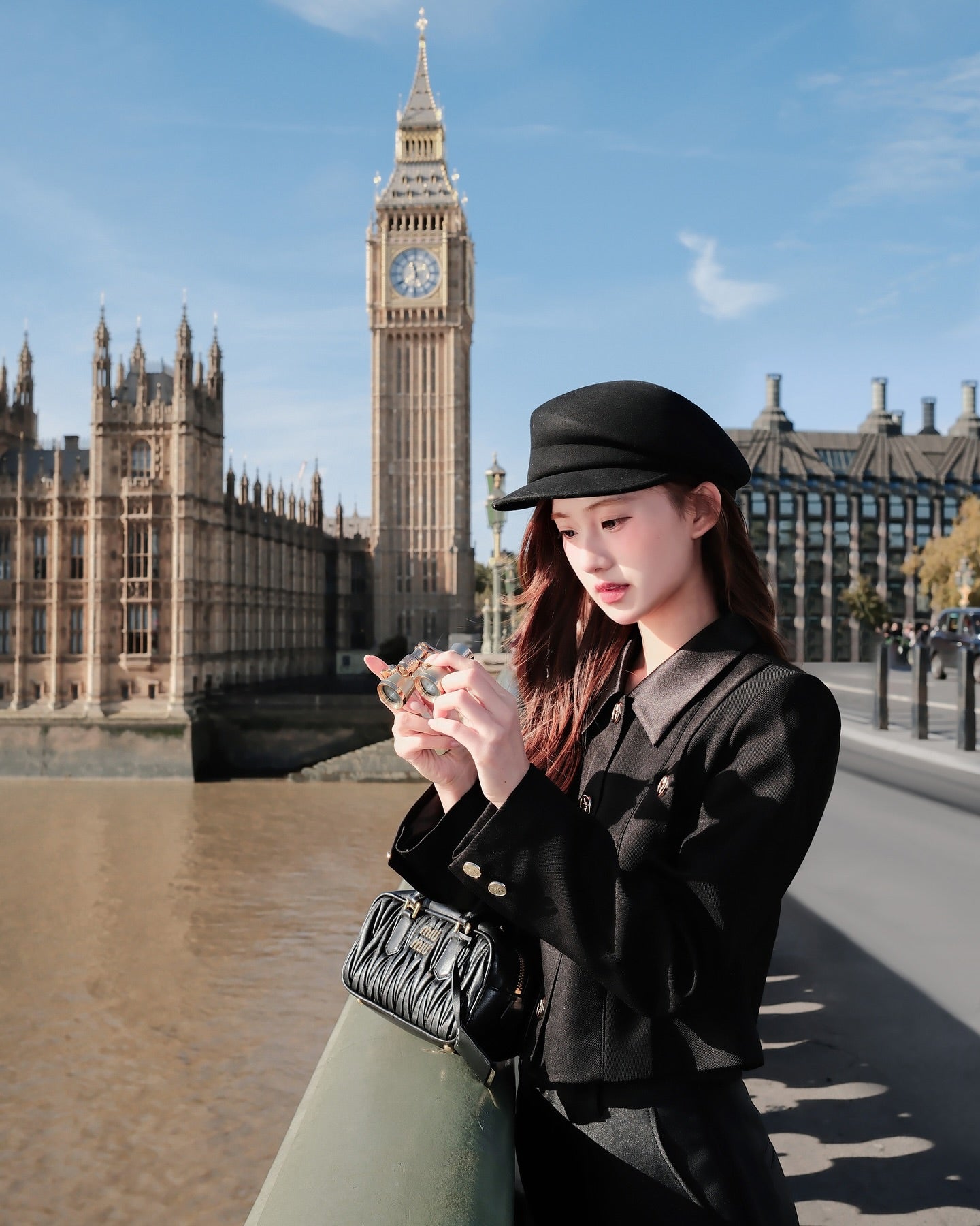 在泰晤士河畔，一位身穿 Grace Little Jacket 🖤新品優惠至 12 月 5 日，來自 lookbook.select--軍裝風短版西裝剪裁和絲綢拼接--的女士瞥了一眼她的手機，而她身後的大本鐘和國會大廈高聳入雲。.