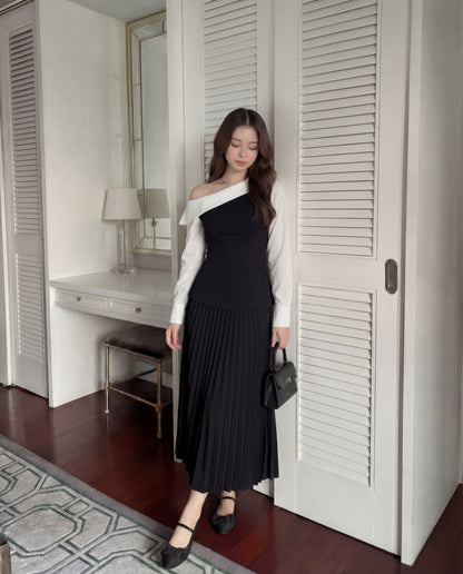 一位女士站在室內，靠近白色的書桌和衣櫃，穿著 the.lookbook.select 的 Mono Skirt Set 🖤新品優惠 2 件 9 折 - 一件露肩黑白上衣搭配黑色百褶裙，再搭配黑色平底鞋和黑色小手包。.