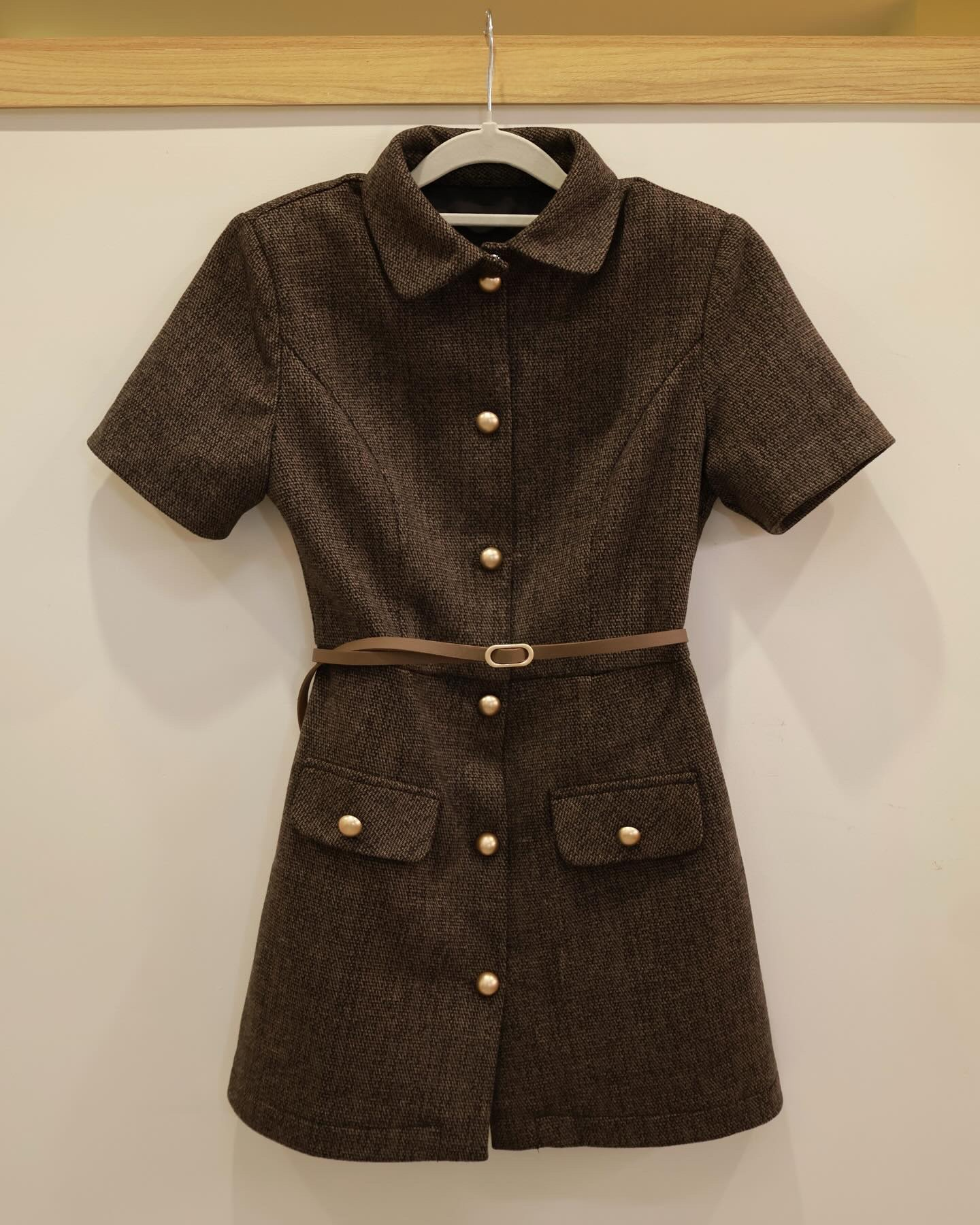 The.lookbook.select的Moka粗花呢連衣裙採用短袖、衣領、金色鈕扣、兩個前口袋和棕色細腰帶。陳列在衣架上，襯以素雅的淺色背景。🖤新品優惠2件9折.