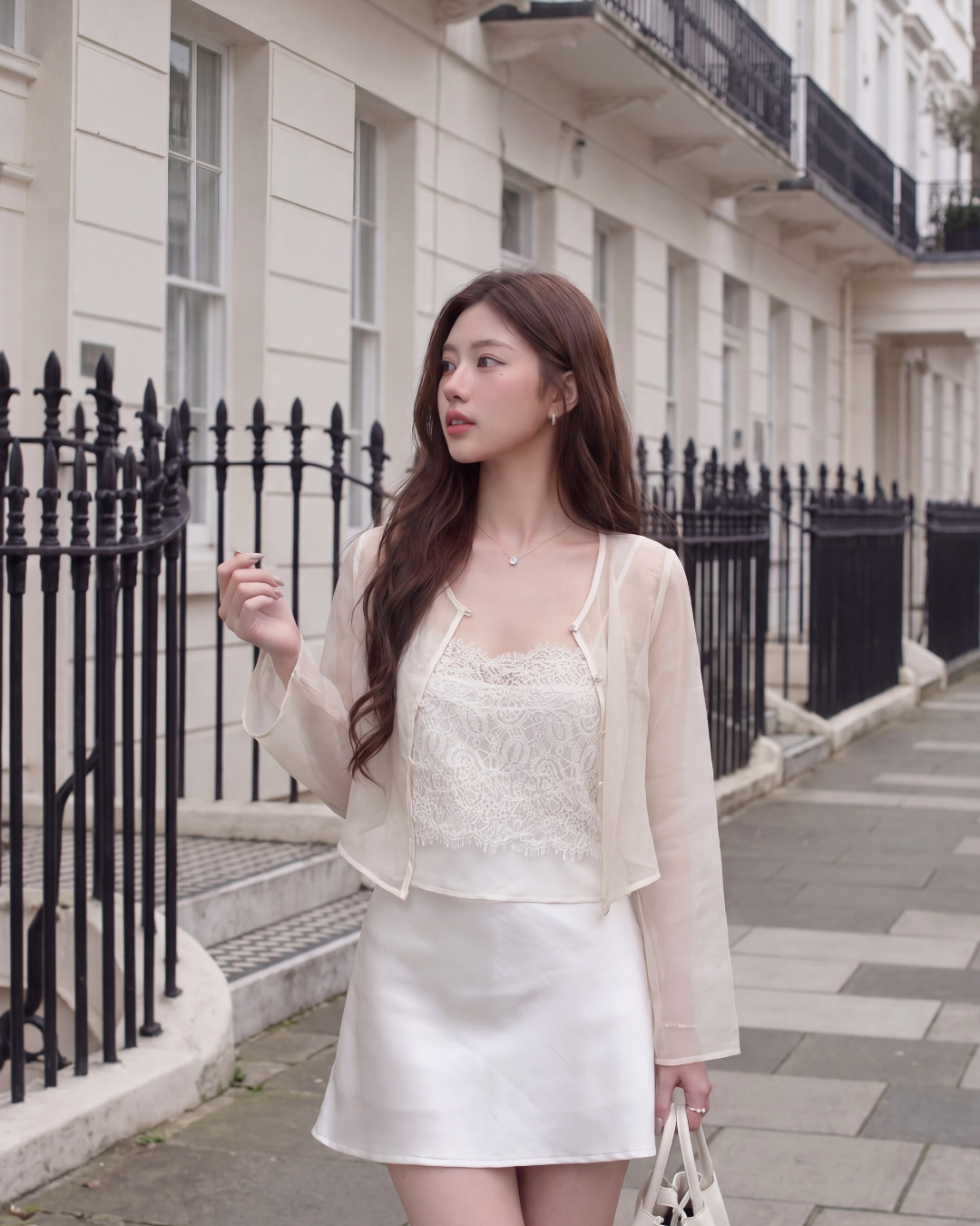 身穿 the.lookbook.select 雪紡 Arch Duo (Cami & Jacket) 的女性站在城市的人行道上，附近是黑色的欄杆和乳白色的建築物，手拿白色手提包。.