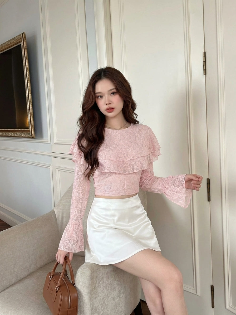 一位身穿 the.lookbook.select 品牌「Spring Muse」蕾絲上衣、搭配白色裙子的女子，坐在一張米色椅子上，左手拿著一個棕色手提包，身處一間光線充足、氣質優雅的房間裡。.