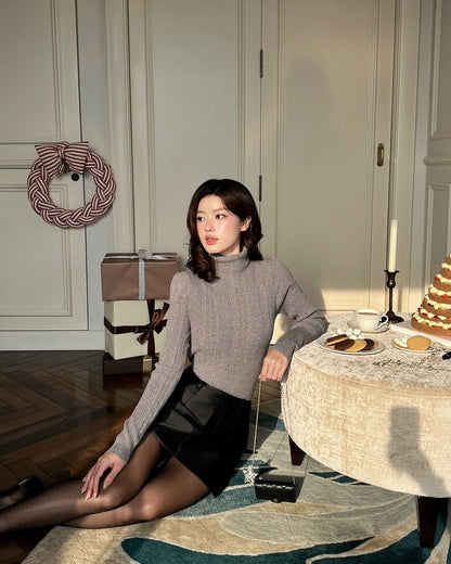 一位身穿 Twinkle Knit Top❄️ 新品優惠 by the.lookbook.select 和黑色短裙的女士坐在地板上，旁邊是一張擺放著甜點、蠟燭、包裝好的禮物和花環的節日餐桌，在明亮的房間裡。.